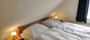 A bedroom with a wooden bed, two bedside lamps, and a window with curtains.
