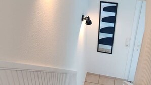 A hallway with a white door, a wall-mounted light, and a framed abstract artwork.