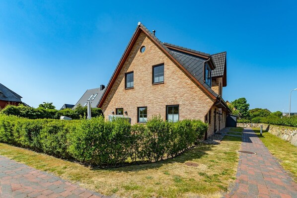 A modern two-story house with a brick exterior, a sloped roof, and a small circular window on the second floor.