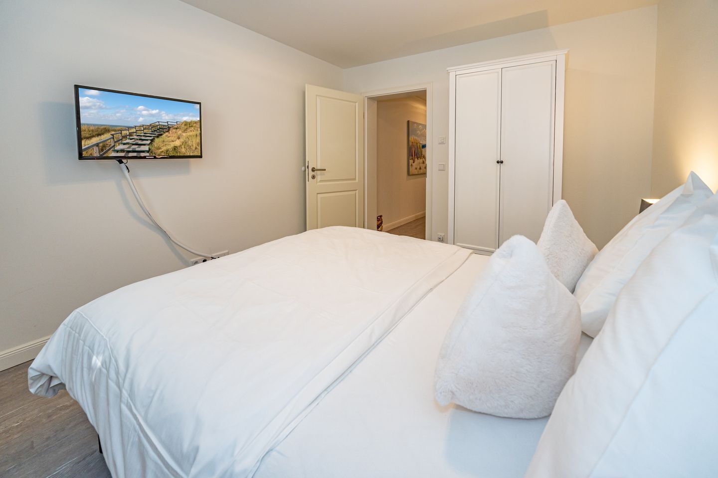 Ein Schlafzimmer mit einem großen Bett, einem an der Wand montierten Fernseher und einer Tür zu einem anderen Raum.