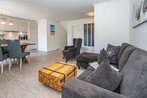 A modern living room with a grey sofa, a wooden coffee table, and a dining area with a table and chairs.