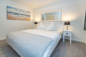 A bedroom with a bed, two bedside tables, a nightstand, a mirror, and a painting on the wall.
