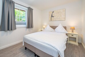 Quarto com cama, duas mesas de cabeceira com luminárias, janela com cortinas e uma obra de arte na parede.