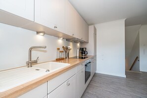 Eine moderne Küche mit weißen Schränken, einer Holzarbeitsplatte, Edelstahlgeräten und einem eingebauten Backofen.