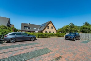 Een oprit met twee geparkeerde auto's, een huis met schuin dak en een heldere blauwe lucht.