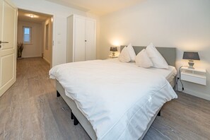 Ein Schlafzimmer mit einem großen Bett, Nachttischlampen und einer Tür zu einem anderen Raum.