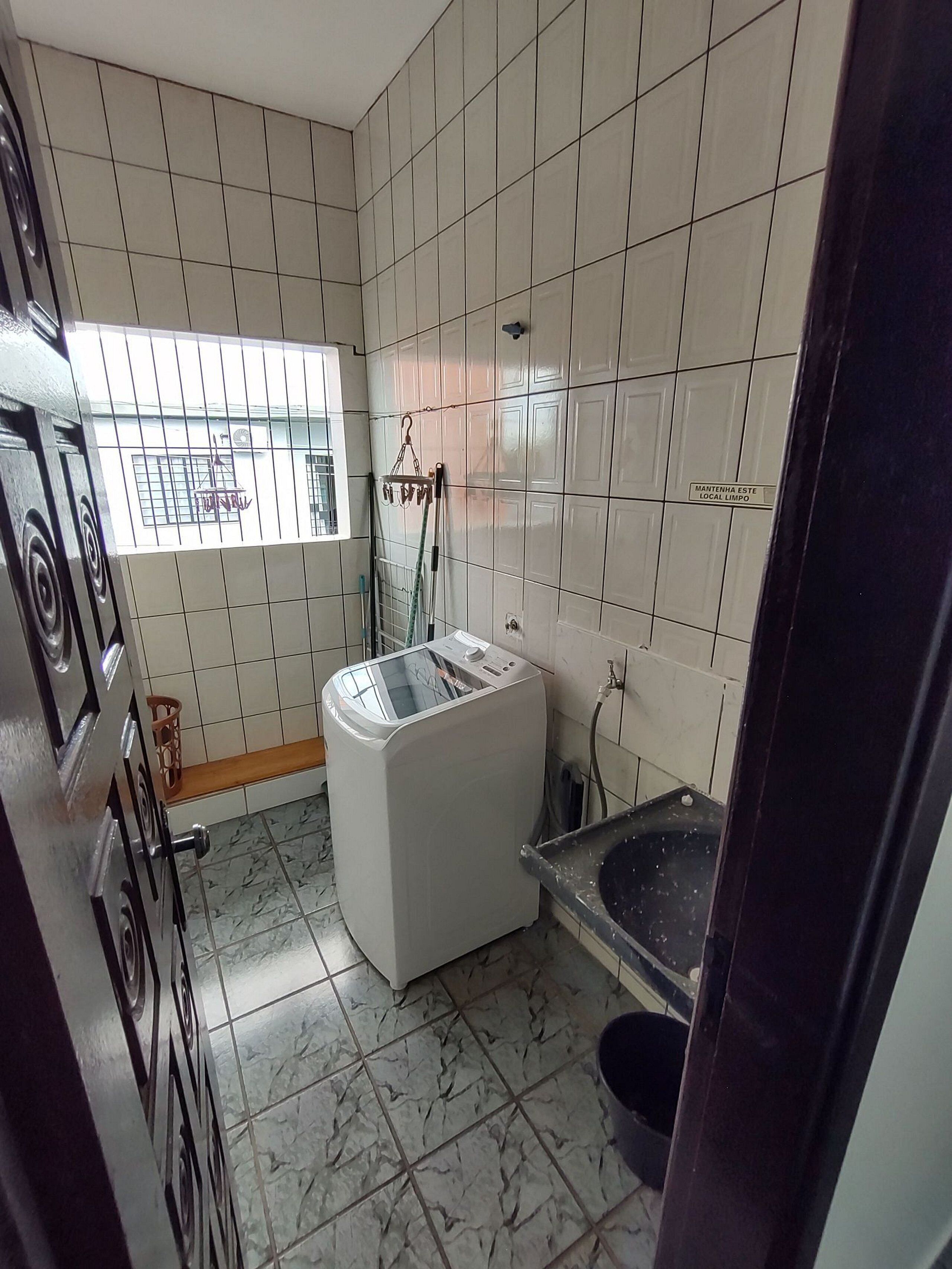 A bathroom with white tiled walls, a white washing machine, a bathtub, and a window with bars.