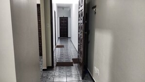 A hallway with a tiled floor, a door at the end, and a wall-mounted light fixture.
