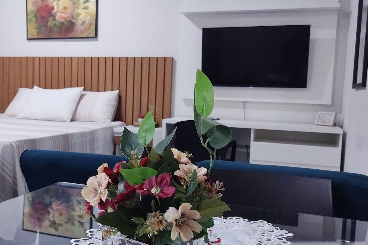 A hotel room with a bed, a TV, a table with a vase of flowers, and a chair.
