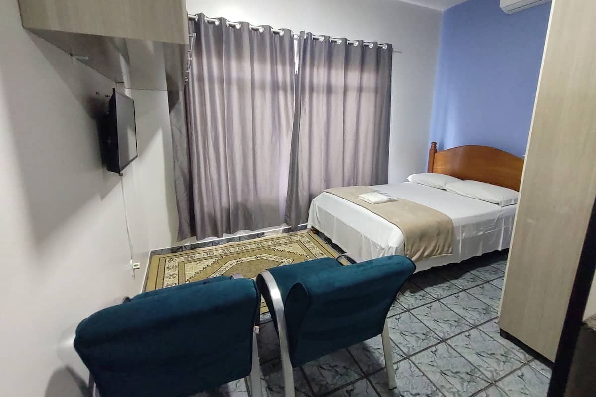 A small hotel room with a bed, a chair, a television, and a curtain.