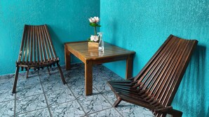 A corner with two wooden chairs and a small table, a decorative flower, and a textured turquoise wall.