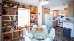 Una cucina moderna con mobili bianchi, un tavolo da pranzo in vetro e diversi oggetti decorativi sugli scaffali.