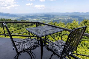 Enjoy a panoramic view of rolling hills and distant mountains from this balcony with a table and two chairs.