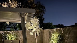 En patio med pergola, bænk og en lille have med sten og planter.