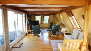 A cozy cabin interior with wooden floors, a large sliding glass door, and a seating area with chairs and a sofa.