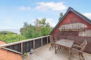 A wooden deck with a table and chairs, overlooking a body of water and greenery.