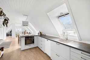A modern kitchen with white cabinetry, a black countertop, and a skylight.