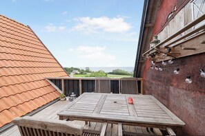 Eine Holzterrasse mit Tisch und Stühlen, mit Blick auf einen Garten und ein Gebäude mit rotem Dach.