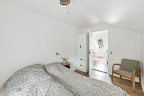 A bedroom with a bed, a chair, a bedside table with a plant, and a wardrobe.