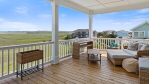 A covered porch with a wooden deck, wicker furniture, and a view of a green landscape. - "DemmMarsh-Uns" is a 4 Bedroom, 3.5 Bathroom Home w/ a Private Pool and Elevator! (Holden Beach)