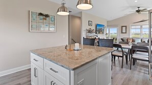 A kitchen with a granite countertop, white cabinetry, pendant lights, and a dining area with chairs and a table. - "DemmMarsh-Uns" is a 4 Bedroom, 3.5 Bathroom Home w/ a Private Pool and Elevator! (Holden Beach)