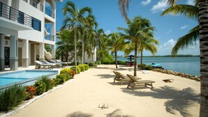 Een zwembadterras van een resort met ligbedden, palmbomen en uitzicht op zee.