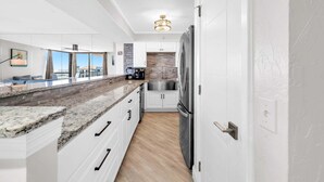 A modern kitchen with white cabinetry, granite countertops, and a stainless steel refrigerator.