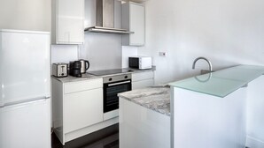 A compact kitchen with white cabinetry, a stainless steel range hood, a built-in oven, a microwave, a toaster, and a glass-fronted sink. - Stunning 2BR in East London, nr Old Street stasion, by Blueground (London)