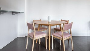 A round wooden table with four chairs, a white vase, and a metal shelf against a plain wall. - Stunning 2BR in East London, nr Old Street stasion, by Blueground (London)