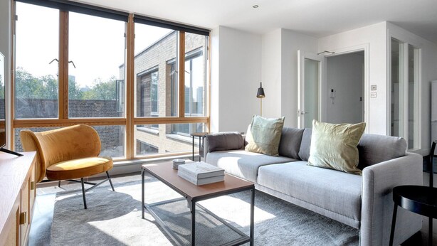 A modern living room with large windows, a sofa, a chair, and a coffee table. - Stunning 2BR in East London, nr Old Street stasion, by Blueground (London)