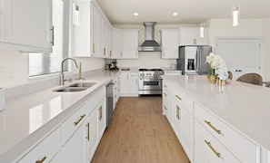 A modern kitchen with white cabinetry, stainless steel appliances, and a wooden floor.