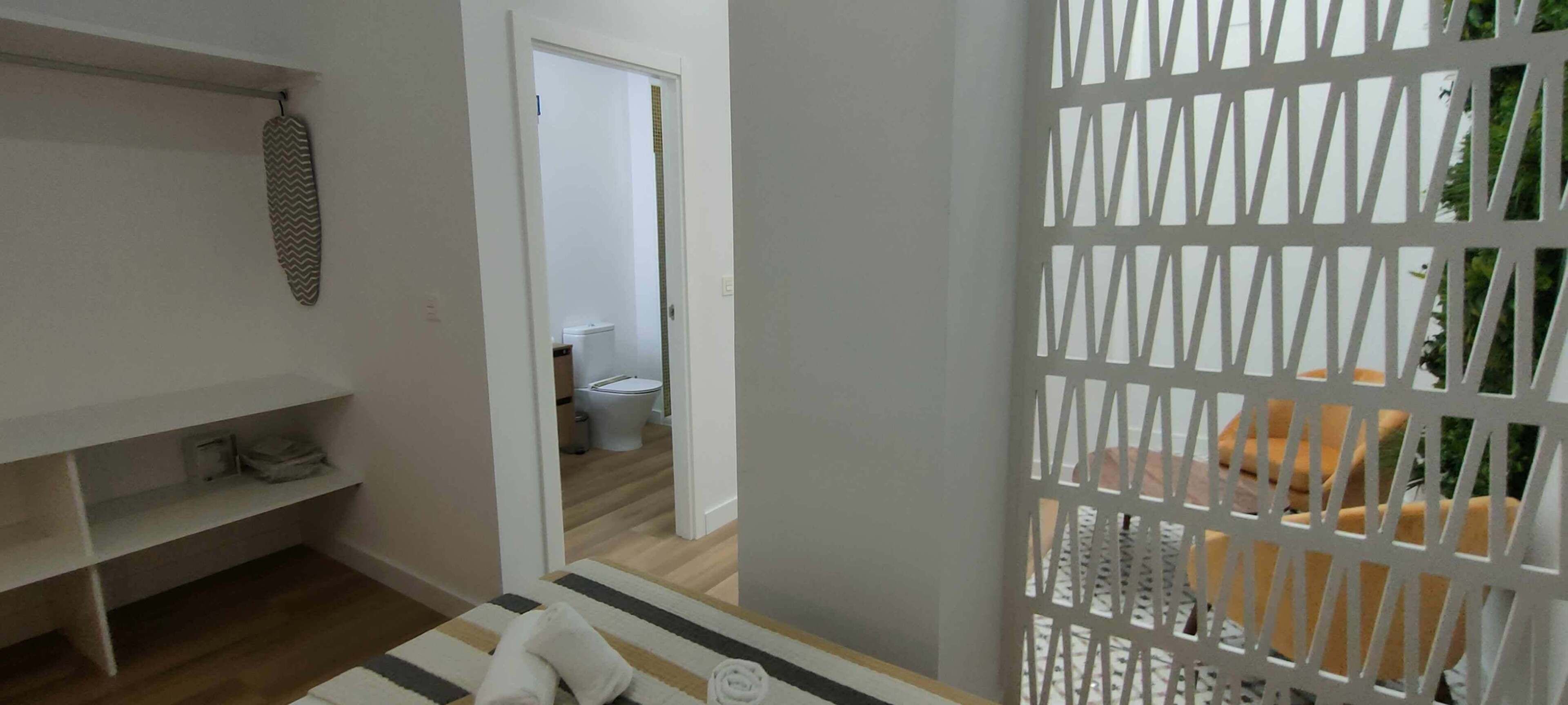 A room with a wooden floor, a striped rug, a white towel, a hanging iron, and a white partition with a geometric pattern.
