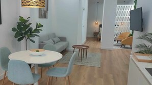 Uma sala de estar moderna com uma mesa de jantar redonda, cadeiras azul claras, um sofá cinza e uma planta verde grande.