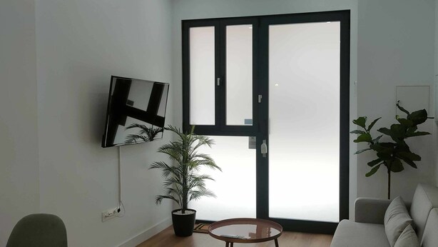 Uma sala de estar com sofá, televisão, planta em vaso e porta de correr de vidro.