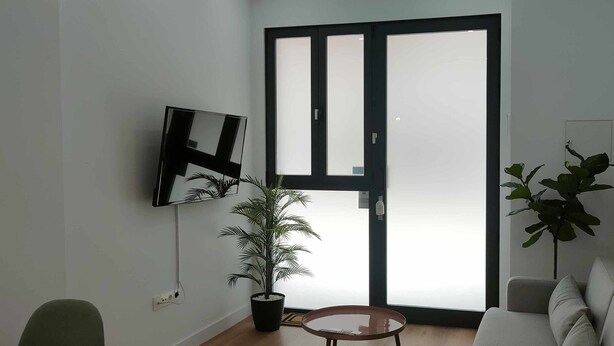 A living room with a sofa, a TV mounted on the wall, a potted plant, and a sliding glass door. - Carmen Street, Seville, Historic Center B3 (Sevilla)