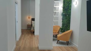 A hallway with a wooden floor, a white wall, a small table with a lamp, and two yellow chairs. - Carmen Street, Seville, Historic Center B3 (Sevilla)