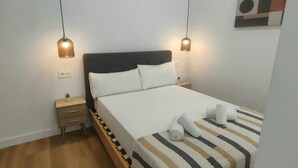 A neatly made bed with white linens and striped bedding, two bedside tables with lamps, and a small potted plant on one table. - Carmen Street, Seville, Historic Center B3 (Sevilla)