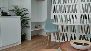A modern kitchen with white cabinets, a sink, and a countertop. There are two light blue chairs around a small round table with a bowl and a remote control. A white decorative screen is in the background. - Carmen Street, Seville, Historic Center B3 (Sevilla)
