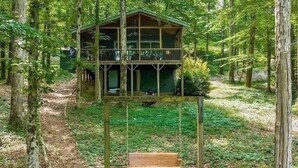 A wooden cabin with a balcony, surrounded by trees in a forest. - Waterfront oasis perfect for couples or fishermen. (Scottsboro)