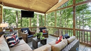 A covered outdoor seating area with wicker furniture, a flat-screen TV, and a view of the forest. - Waterfront oasis perfect for couples or fishermen. (Scottsboro)