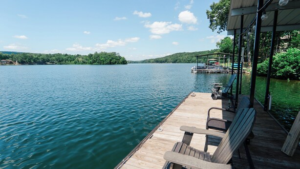Een houten steiger met Adirondack-stoelen en een overdekte zithoek met uitzicht op een kalme rivier.