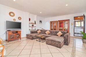 A living room with a sectional sofa, a television, a cabinet, and a window with blinds.