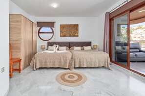 A bedroom with two beds, a large window, a sliding glass door, and a view of the outside.
