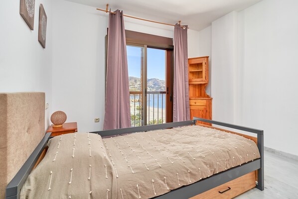 Un dormitorio con cama, un armario de madera, una ventana con cortinas y vistas al exterior.