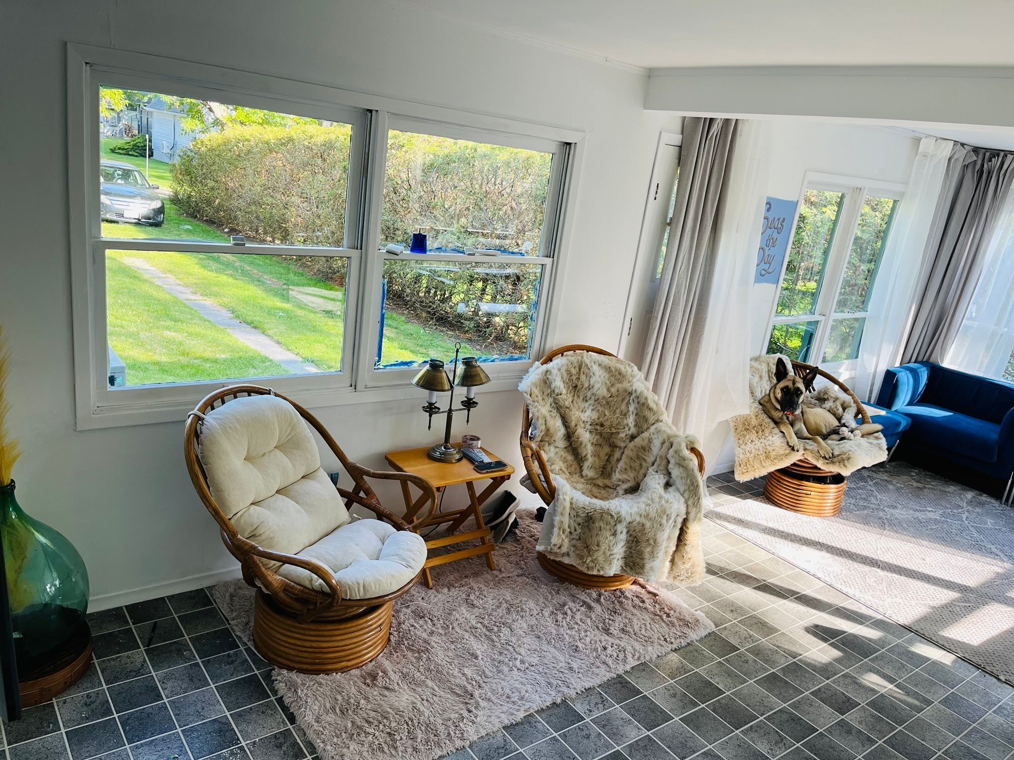 Un salon chaleureux avec des fauteuils en osier, un tapis moelleux et une vue sur un jardin verdoyant grâce à de grandes fenêtres.