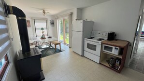A compact kitchen with a stove, microwave, and refrigerator. There is a dining area with a table and chairs, and a small bench. - Lake Huron Getaway: Cozy Cottage, Private Access, Second-Row Location (Dashwood)
