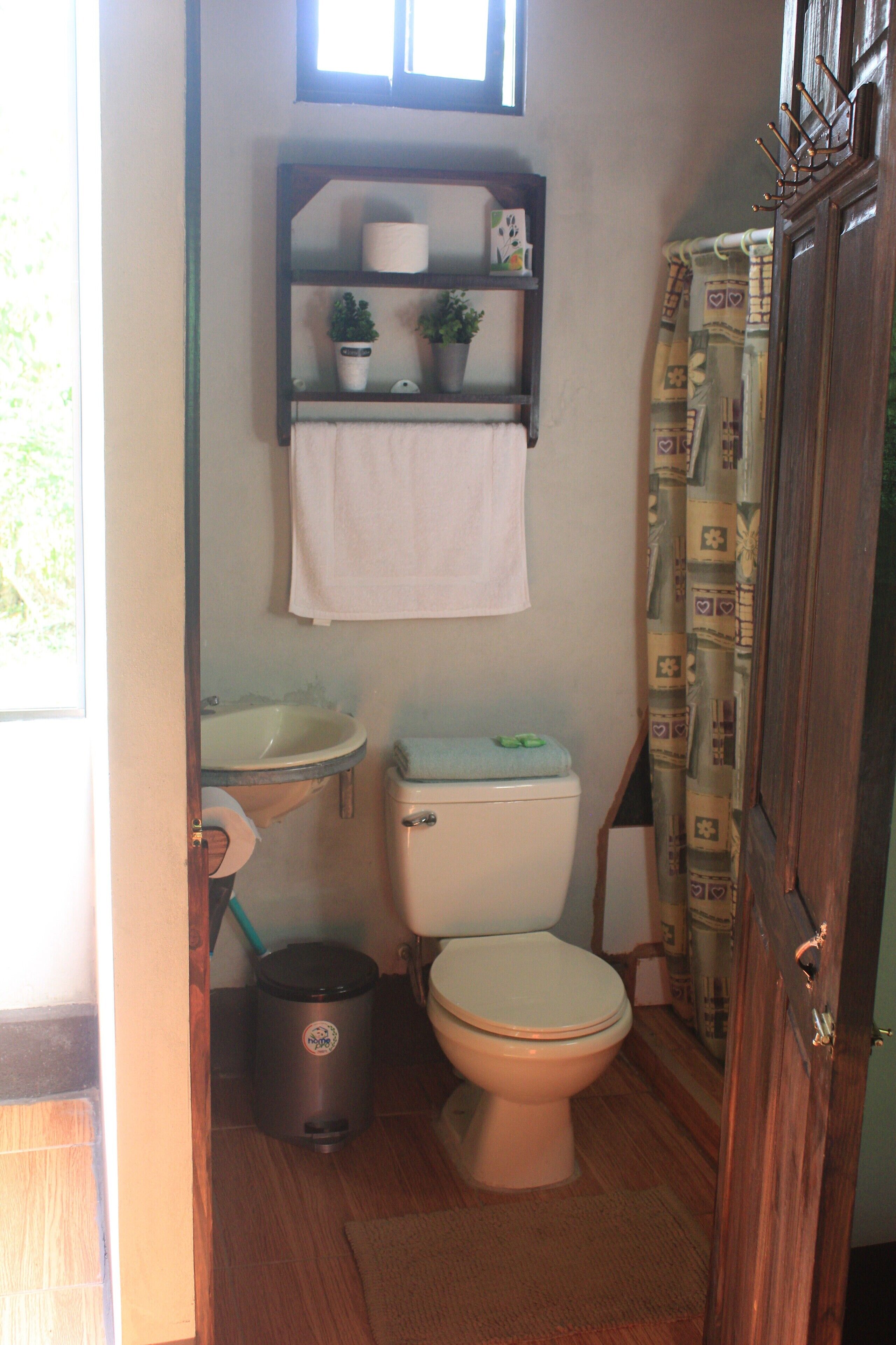 A compact bathroom with a toilet, sink, and shelf above the sink.