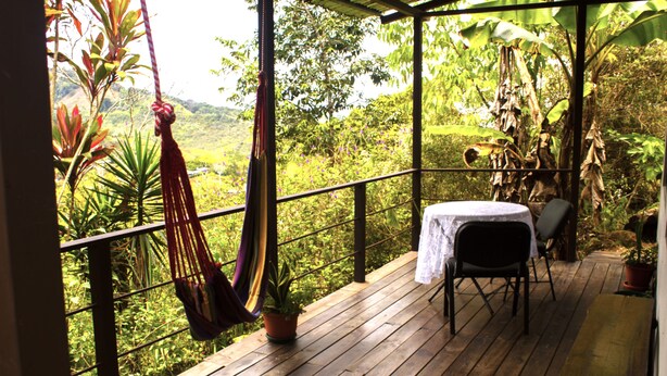A wooden deck with a hammock, a table with a white tablecloth, and chairs. - Cabañas Colibrí Tayutic (Tayutic)