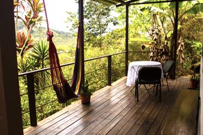 Une terrasse en bois avec un hamac, une table recouverte d’une nappe blanche et des chaises.
