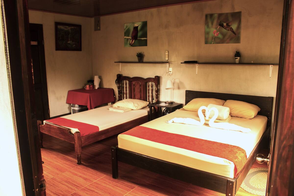 A hotel room with two single beds, a wooden headboard, a red table, and a small nightstand.